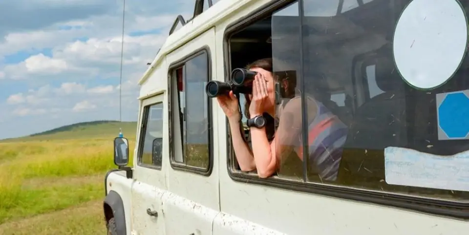 Guest looking through binoculars from the window of a safari vehicle