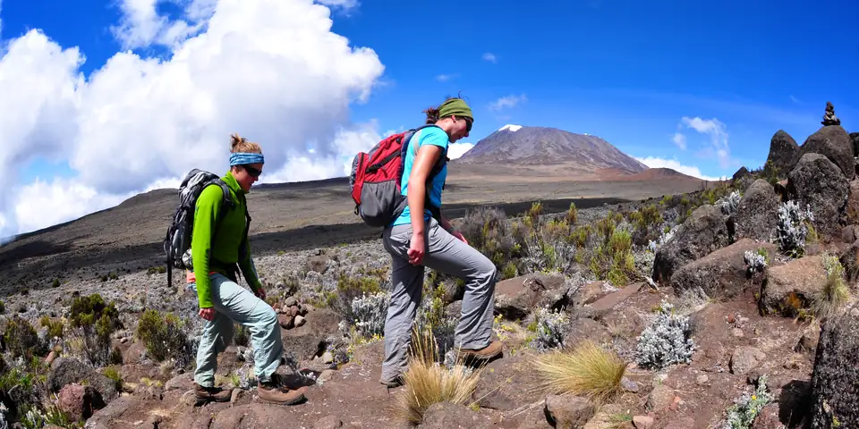 Climbers on a rocky trail with the snow-capped summit of Kilimanjaro behind
