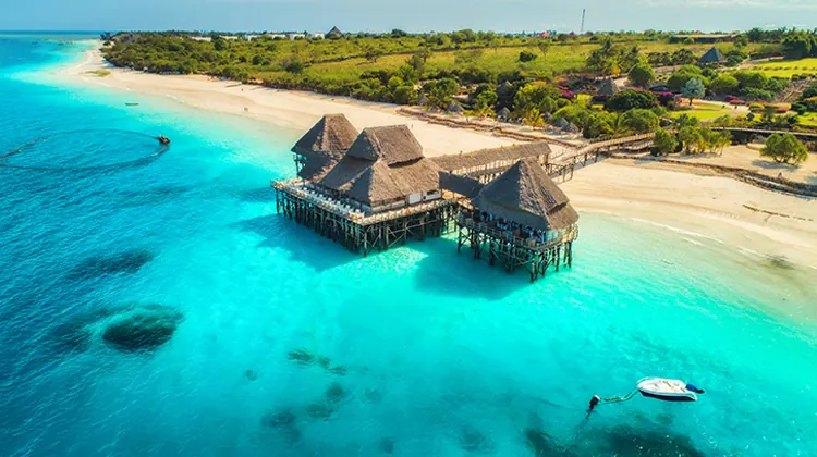 Thatched building on stilts over turquoise water beside a white sand beach on Zanzibar