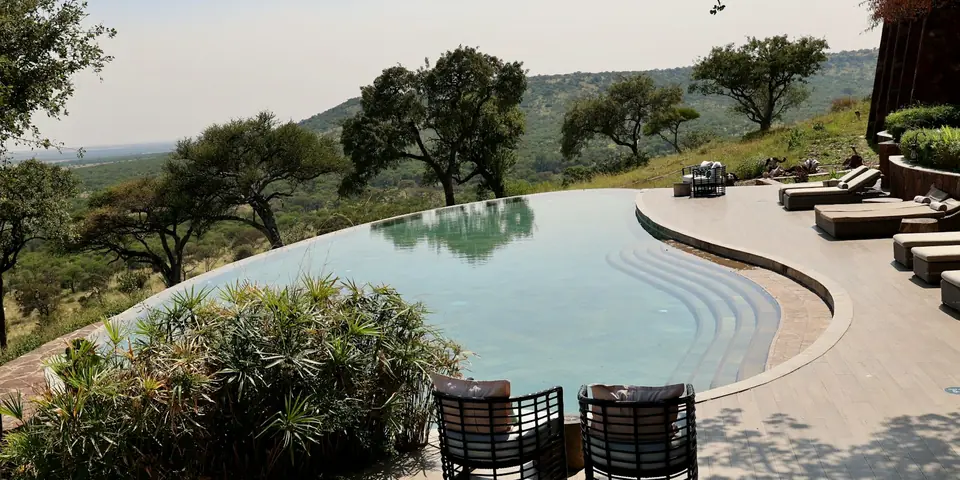 Serengeti safari lodge pool and terrace with loungers, looking out over acacia trees and the plains